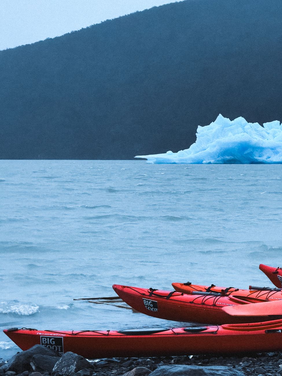 Sea kayaker resting paddle while gazing at massive blue glacial wall